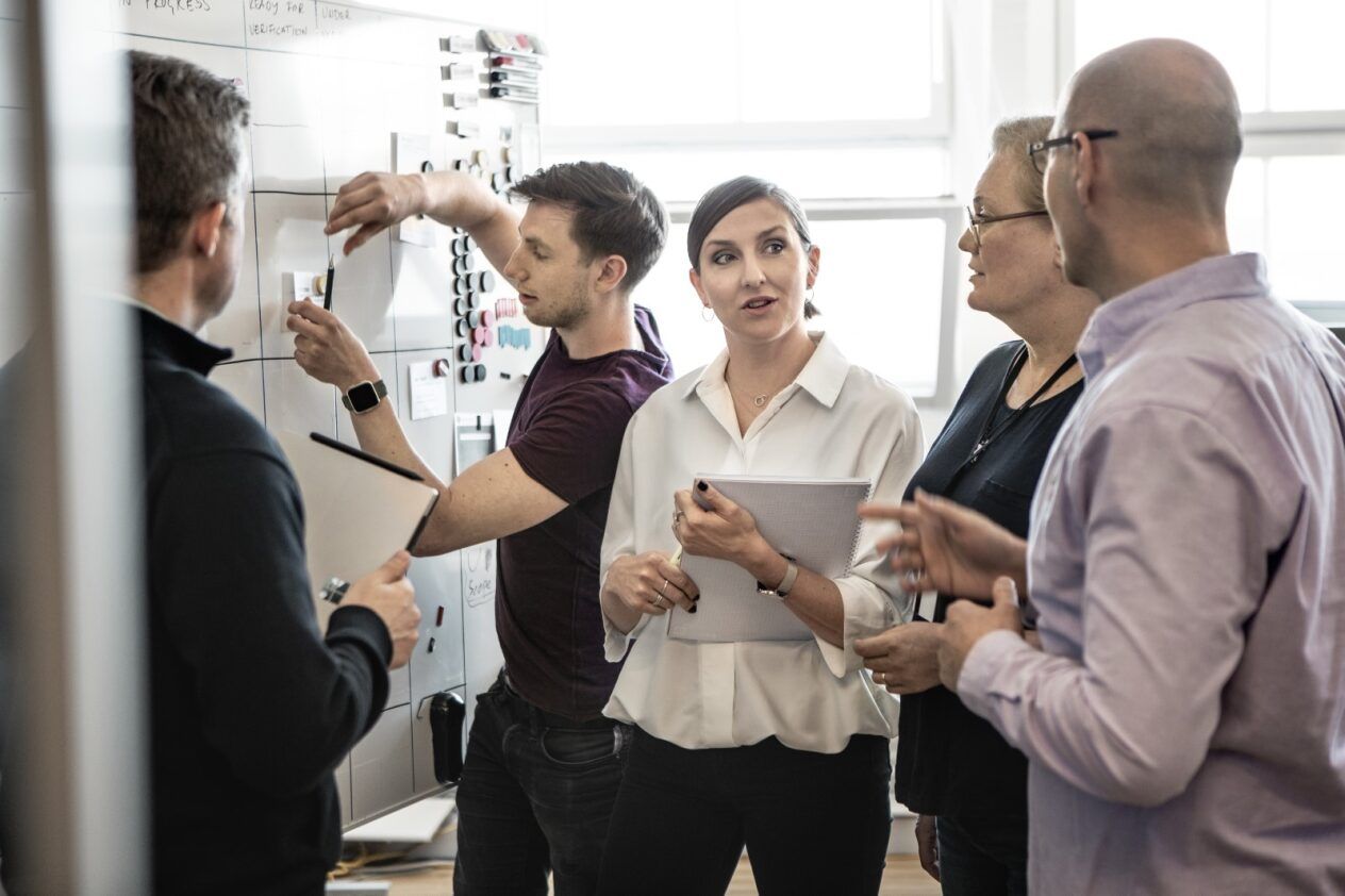 Group of People Stood Talking by a Whiteboard